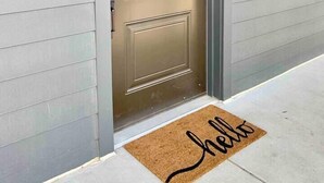 Une porte d’entrée avec un paillasson sur lequel est écrit « bonjour » et le numéro 208 sur le mur.