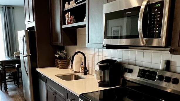 Une cuisine moderne avec des meubles en bois foncé, des appareils électroménagers en acier inoxydable, un four à micro-ondes, une cuisinière et un évier.