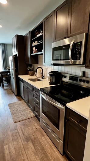Une cuisine moderne avec des meubles en bois foncé, des appareils électroménagers en acier inoxydable, un four à micro-ondes, une cuisinière et un évier.