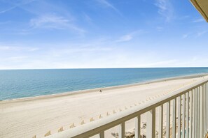 A beach view from a balcony with a railing, clear sky, and calm sea.