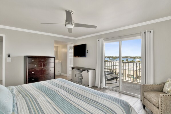 A bedroom with a bed, a dresser, a desk, a TV, and a balcony with a view.