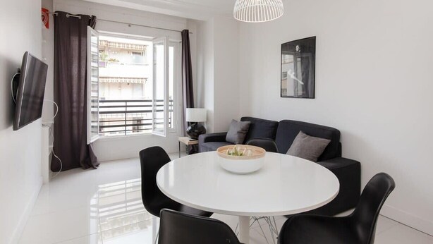 A modern living room with a round dining table, black chairs, a black sofa, a white pendant light, and a TV mounted on the wall. - Modern & cozy 150m from the Croisette (Cannes)