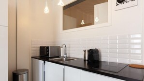A modern kitchen with white cabinets, a black countertop, a stainless steel sink, a coffee maker, and a trash can. - Modern & cozy 150m from the Croisette (Cannes)