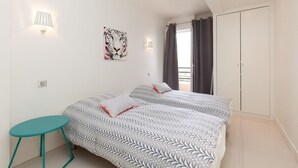 A bedroom with two beds, a small table, a wall-mounted lamp, a tiger artwork, and a wardrobe. - Modern & cozy 150m from the Croisette (Cannes)