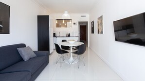 A modern living room with a dark grey sofa, a round dining table with chairs, and a large flat-screen TV mounted on the wall. - Modern & cozy 150m from the Croisette (Cannes)