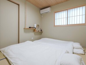 Quarto com cama, janela, aparelho de ar condicionado e prateleira com objetos.