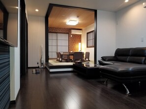 Uma sala de estar moderna com piso de madeira escura, um sofá de couro preto e uma área de jantar com mesa e cadeiras de madeira.