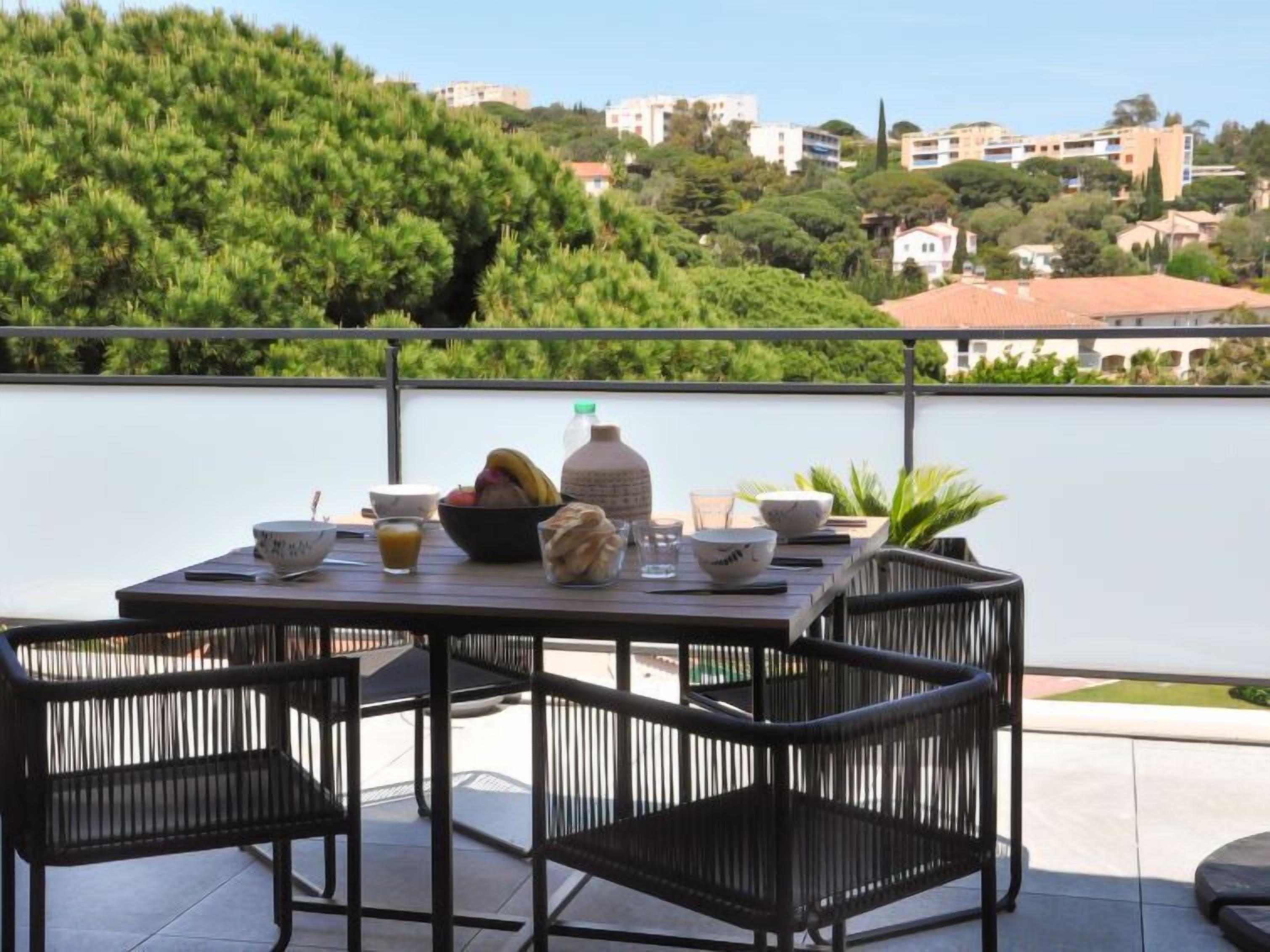 A terrace with a table set for dining, surrounded by chairs, overlooking a hillside with buildings.