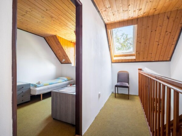 A small, single-room apartment with a sloped ceiling, a bunk bed, a desk, and a chair.