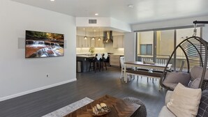 Una cocina moderna con iluminación colgante, una zona de comedor con banco y una sala de estar con sillón colgante.