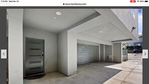 Fachada de una propiedad con puerta gris, garaje y camino de acceso de hormigón.