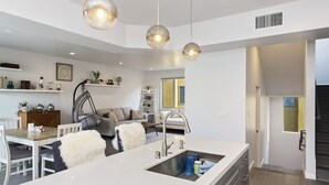 Una cocina moderna con una isla central, iluminación colgante y un comedor con sofá y sillas.