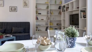 A living room with a sofa, a bookshelf, a TV, and a dining table set with glasses and a pitcher.