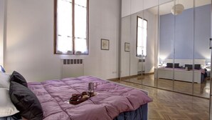 A modern bedroom with a large bed, a glass partition, and a view into another room.