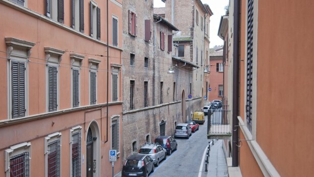 A narrow street lined with historic buildings, parked cars, and a visible parking sign.