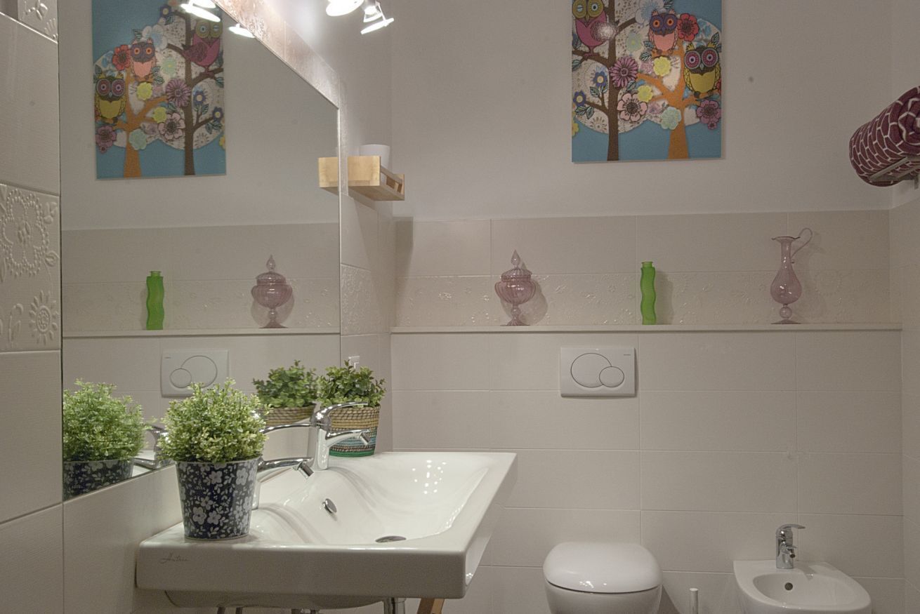 A bathroom with a white sink, two wall-mounted shelves with toiletries, a toilet, and a bidet.