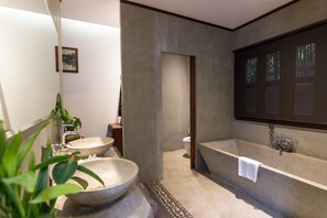 A modern bathroom with two stone sinks, a large bathtub, and a mirror with a projection. - Java Wooden Villa by AIC (Siem Reap)