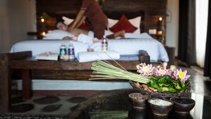 A bedroom with a bed, pillows, and a bedside table with toiletries and flowers. - Java Wooden Villa by AIC (Siem Reap)