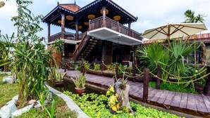 A traditional wooden structure with a balcony and a covered area, surrounded by lush greenery and a small pond. - Java Wooden Villa by AIC (Siem Reap)