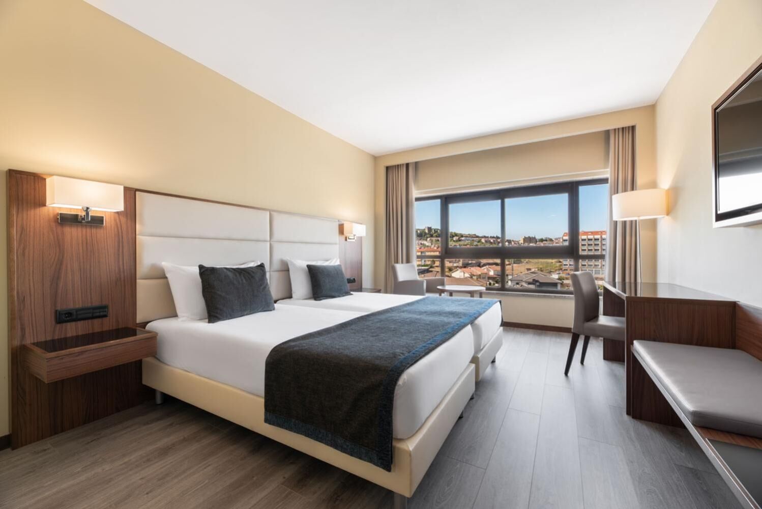 A hotel room with a large bed, a desk, a chair, and a TV.