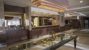 Un hall d’hôtel moderne comprenant un comptoir d’accueil, une vitrine en verre exposant des objets décoratifs et un lustre.