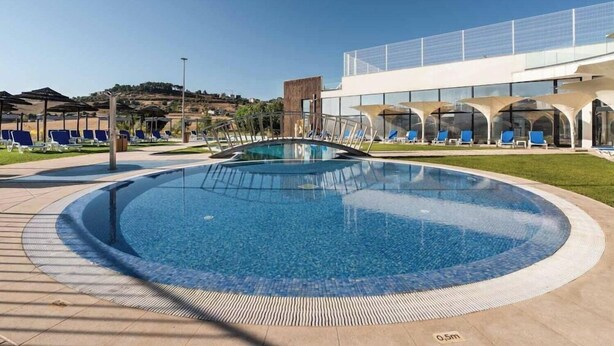 Une piscine circulaire entourée de chaises longues, avec un bâtiment moderne en arrière-plan.