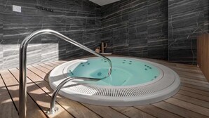 Un bain à remous intérieur moderne, doté d’un robinet métallique élégant, installé sur un mur de marbre foncé et un plancher en bois.
