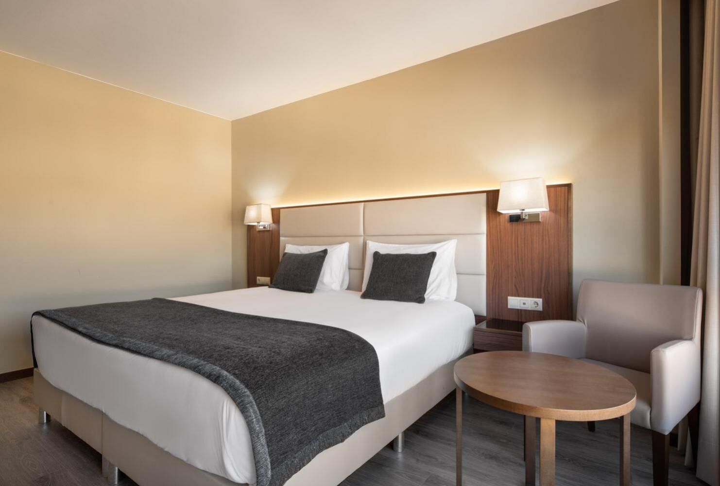 Ein Hotelzimmer mit einem großen Bett, zwei Nachttischlampen, einem kleinen runden Tisch und einem Sessel.