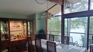 A dining area with a large table, chairs, a chandelier, and a view of a lake through large windows. - Sunset Retreat Lake Rosseau  (Rosseau)