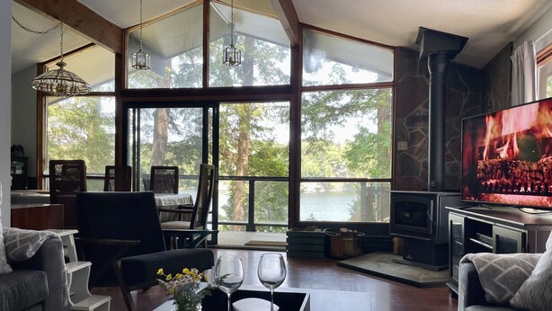 A spacious living room with large windows, a fireplace, and a television. - Sunset Retreat Lake Rosseau  (Rosseau)