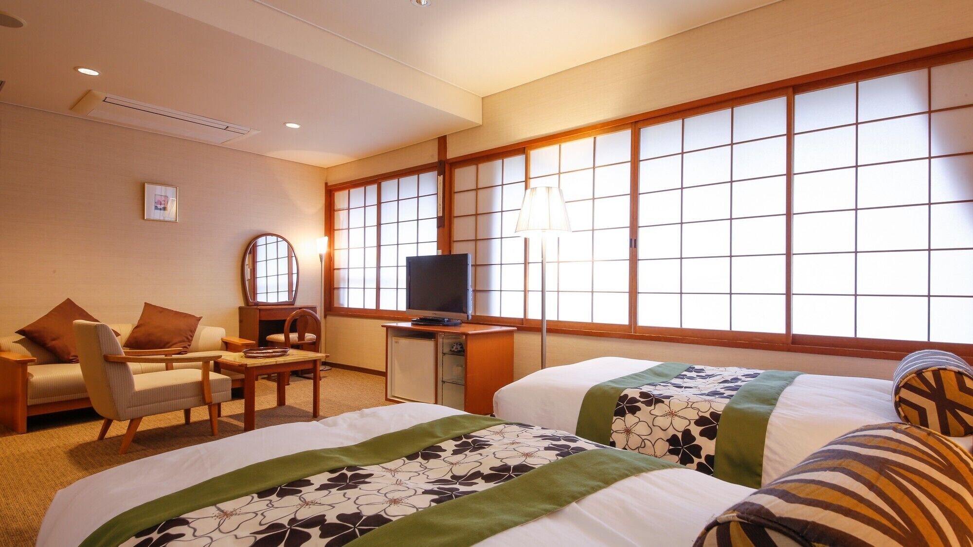 A hotel room with two beds, a desk with a TV, a chair, and a large window with a view.