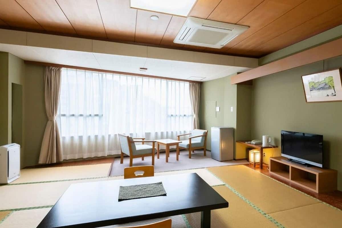 A room with a wooden ceiling, a dining table with chairs, a television on a stand, and a painting on the wall.