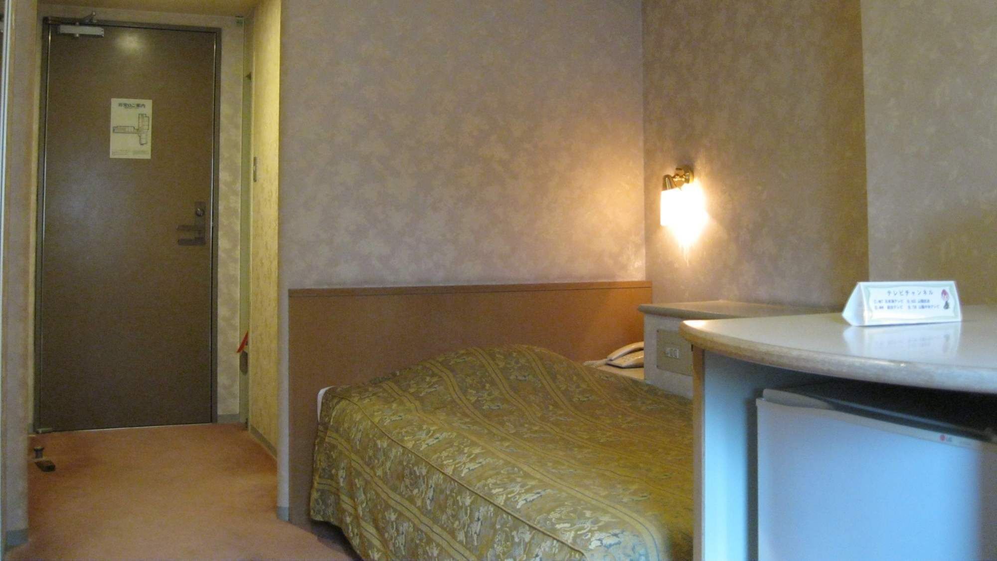 A hotel room with a bed, a desk, a chair, a telephone, and a door.