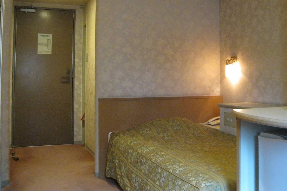 A hotel room with a bed, a desk, a chair, a telephone, and a door.