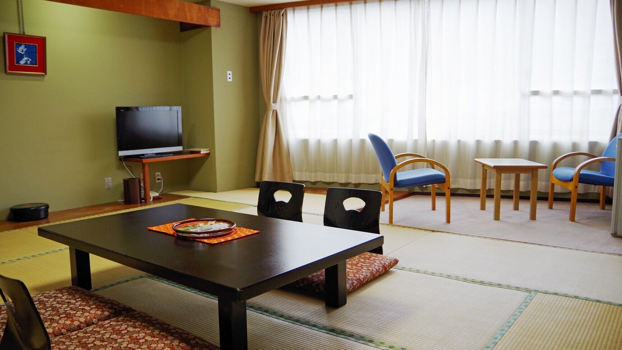 A living room with tatami flooring, a television, and a dining table with chairs.