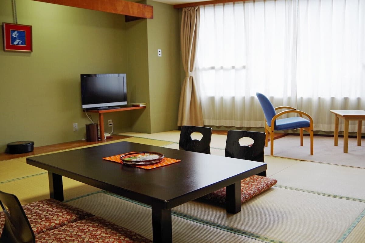 A living room with tatami flooring, a television, and a dining table with chairs.
