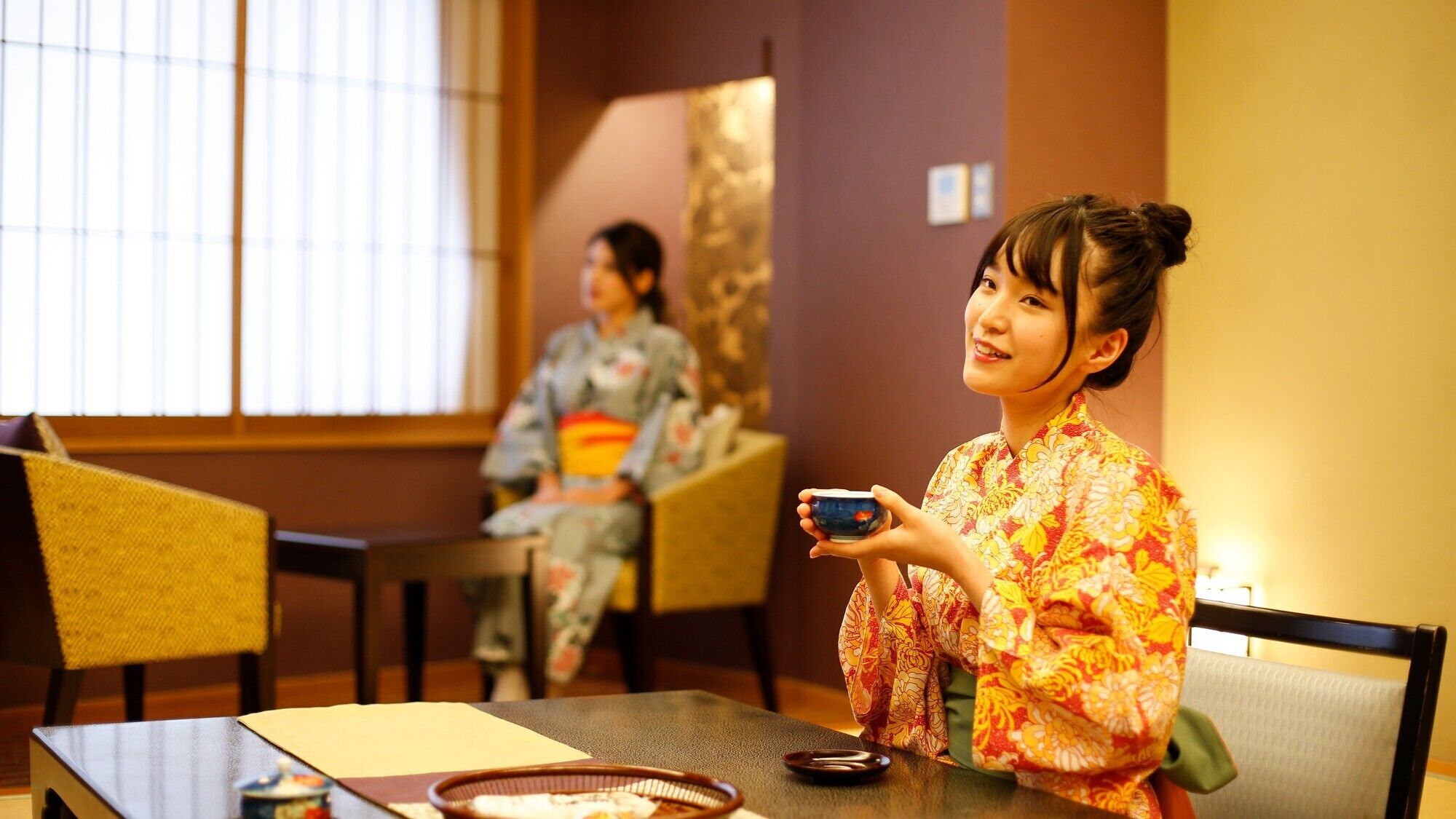 A traditional Japanese room with tatami flooring, a low table, and a window with vertical blinds.