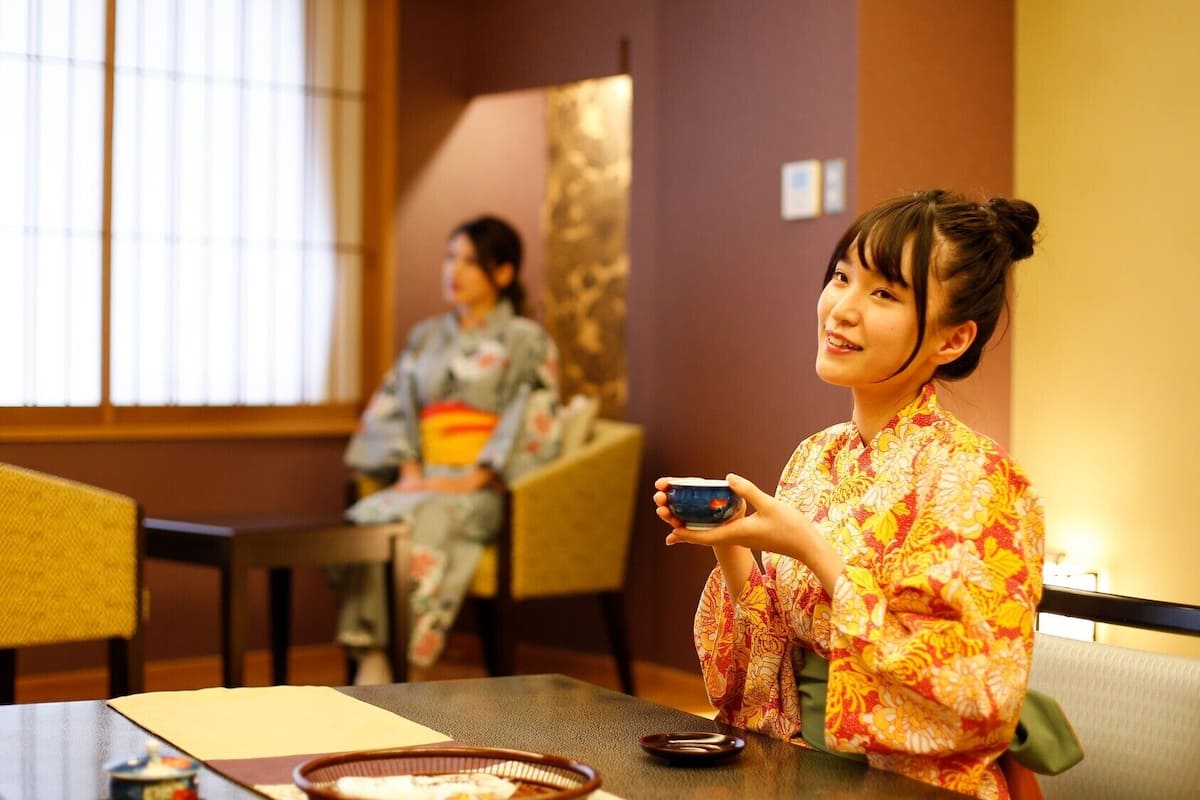 A traditional Japanese room with tatami flooring, a low table, and a window with vertical blinds.