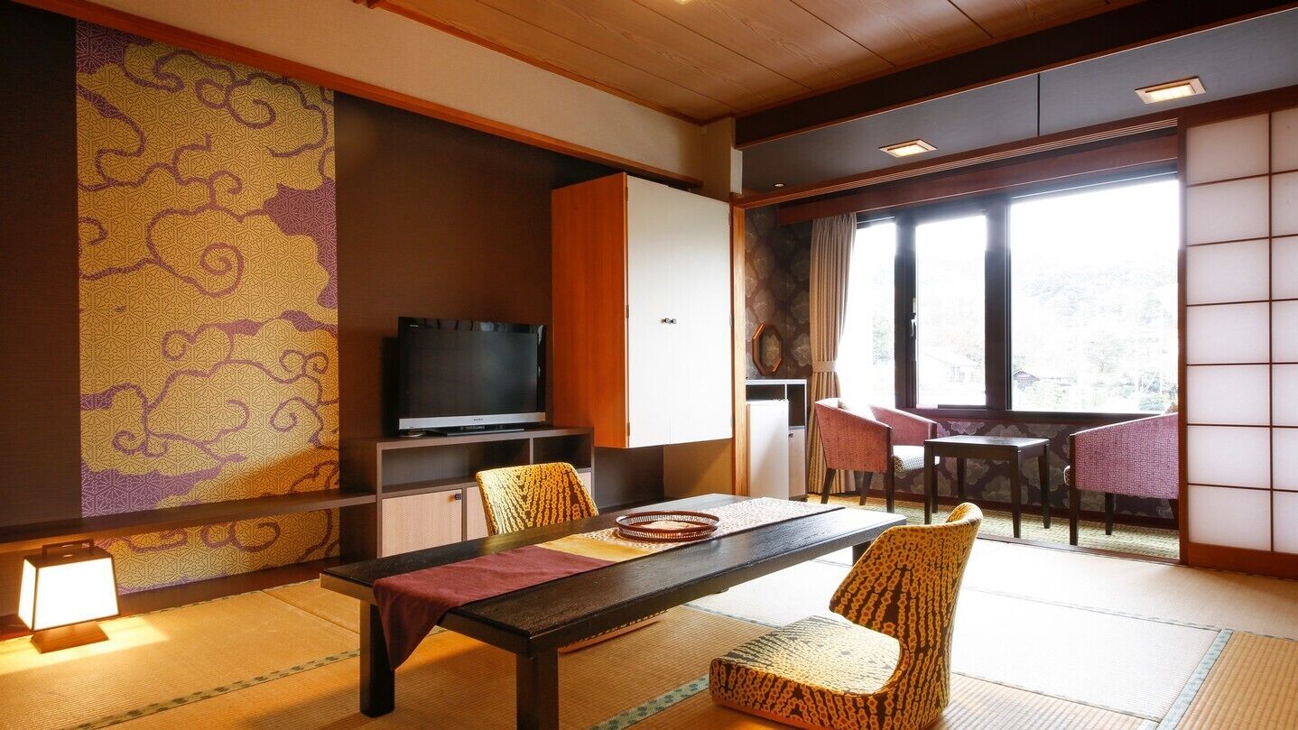 A traditional Japanese-style room with tatami flooring, a low table with cushions, a television, and a sliding door leading to a balcony.