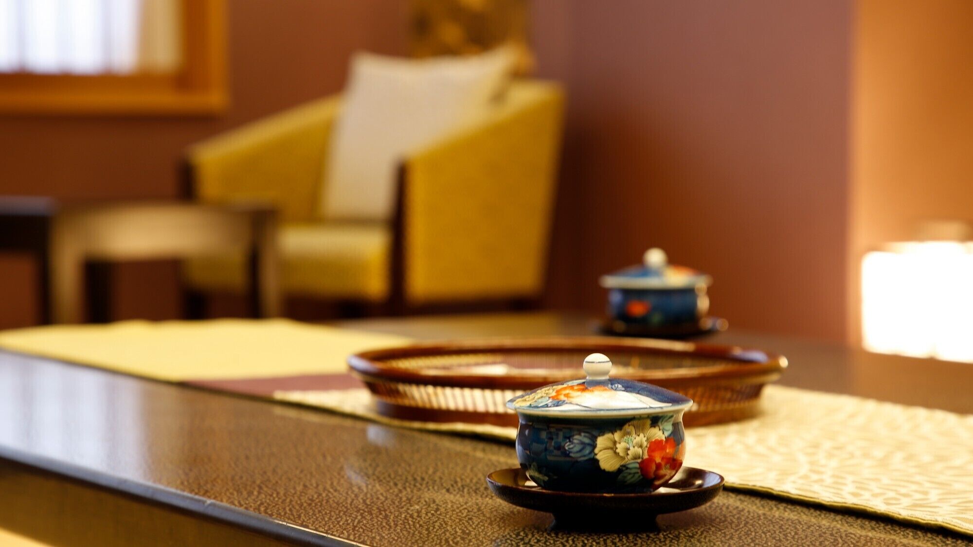 A table with a teapot and a cup, a tray, and a chair in the background.