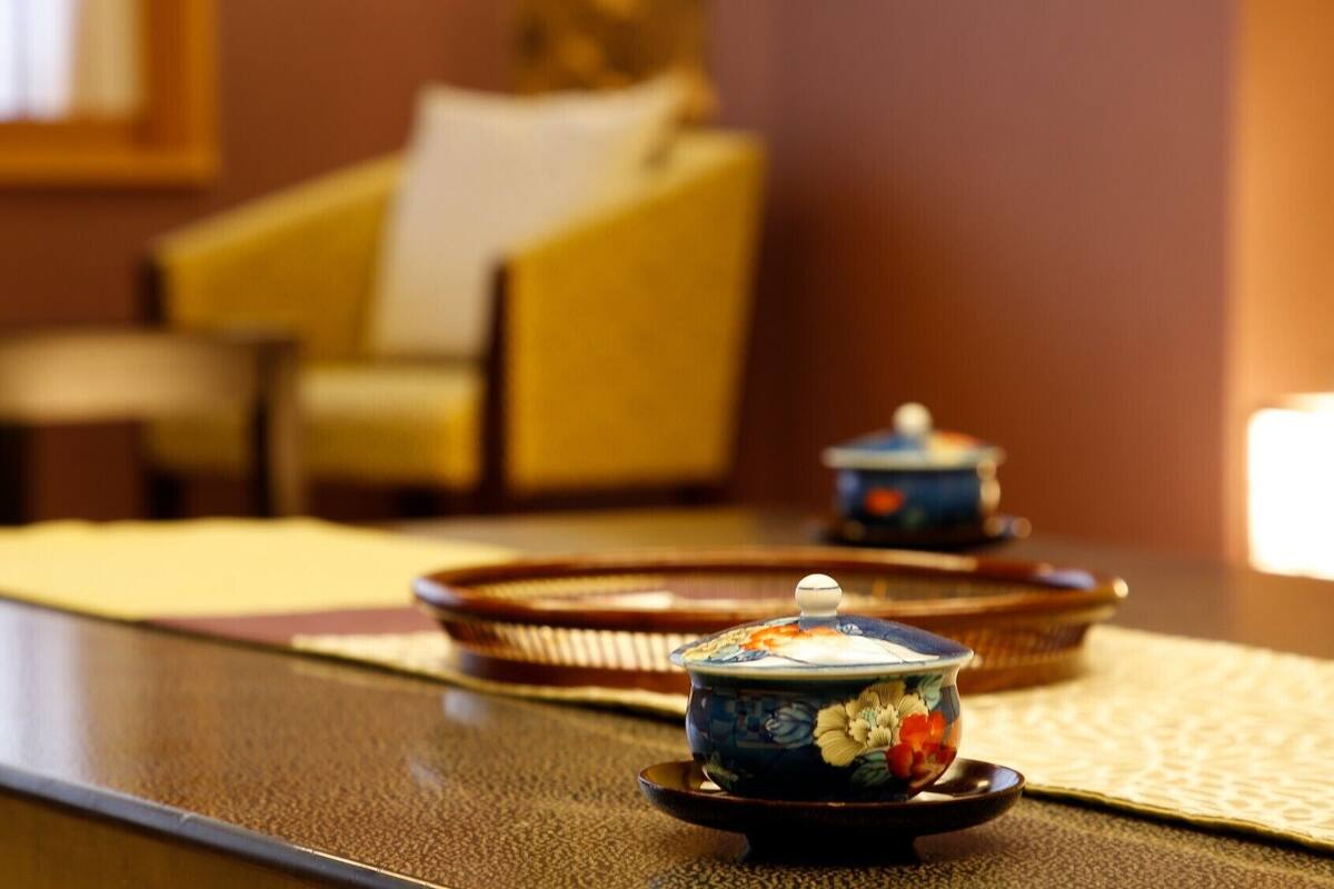 A table with a teapot and a cup, a tray, and a chair in the background.