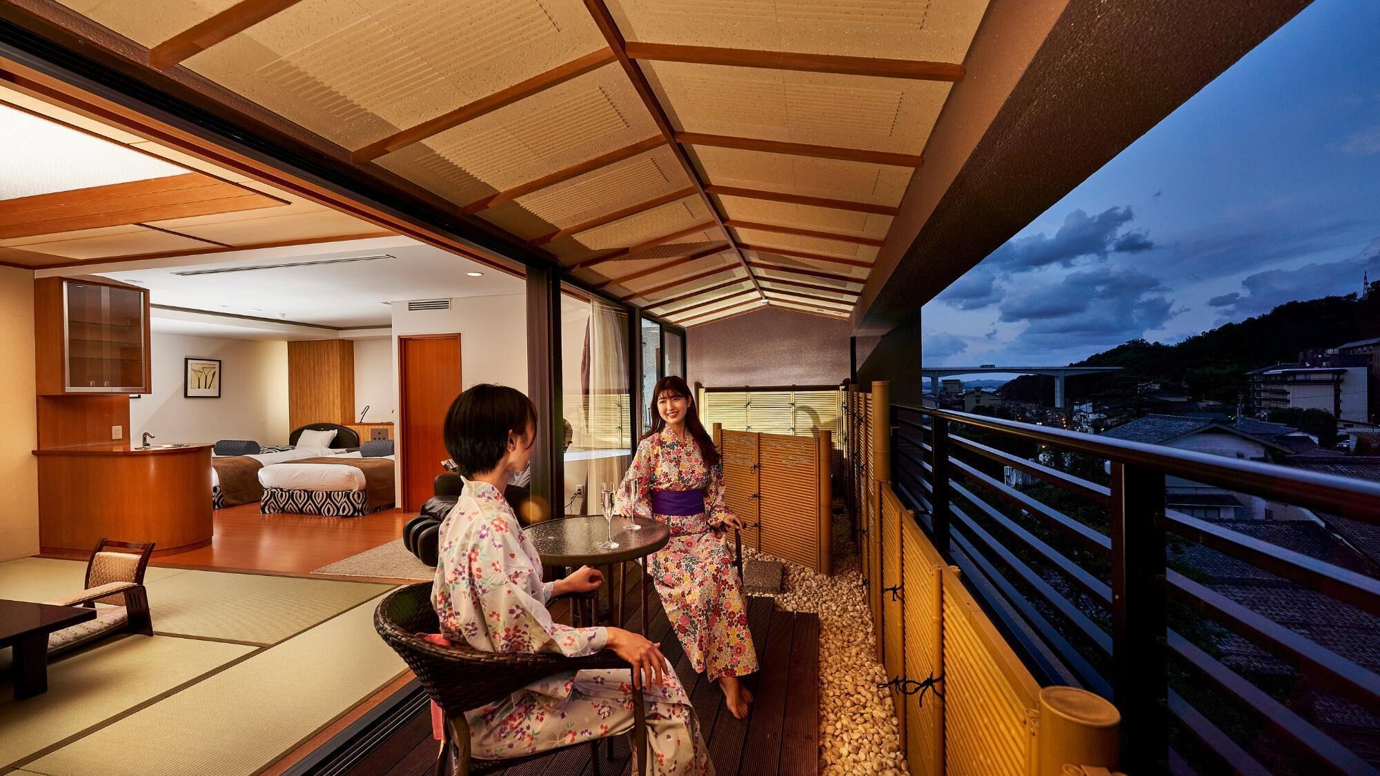 A room with a bed, a sitting area, and a balcony with a view of the city.