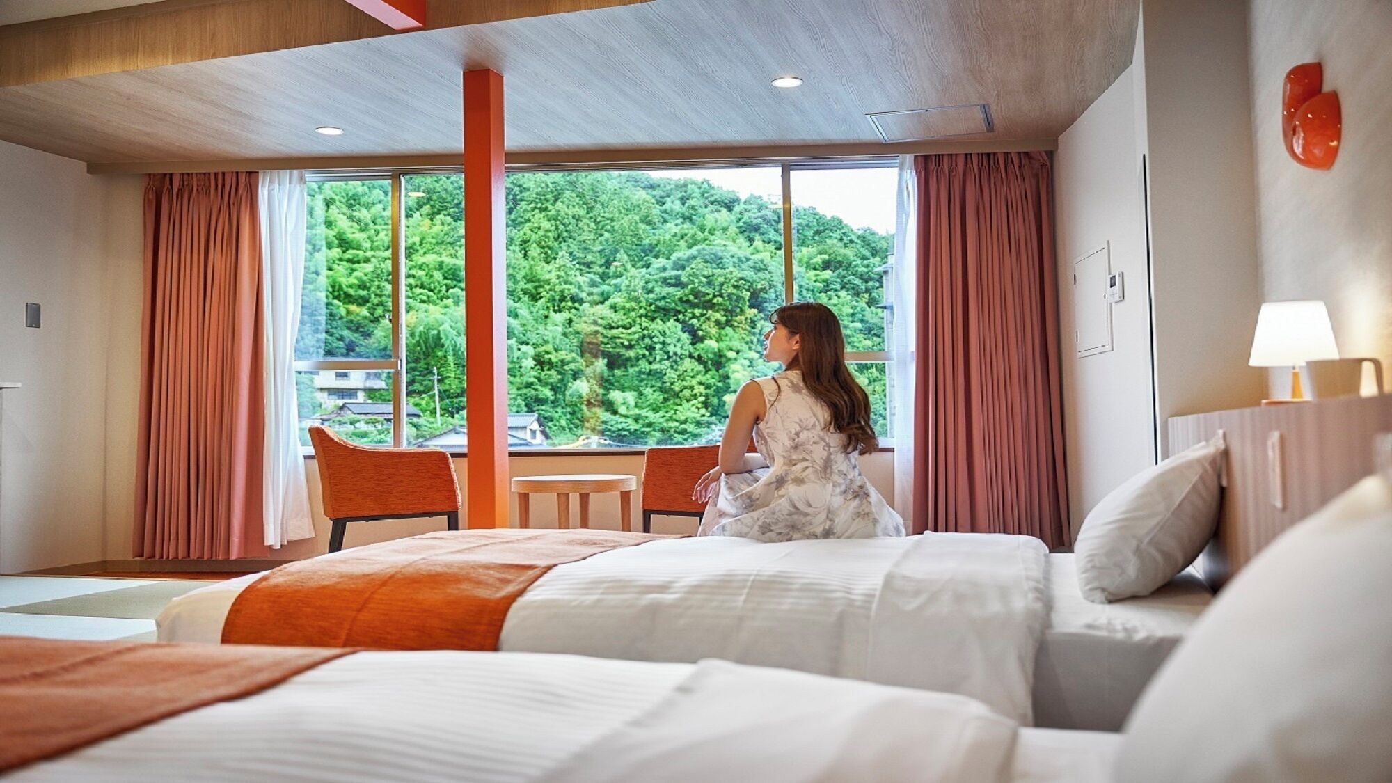 A hotel room with a bed, a chair, a table, and a large window with a view of greenery.