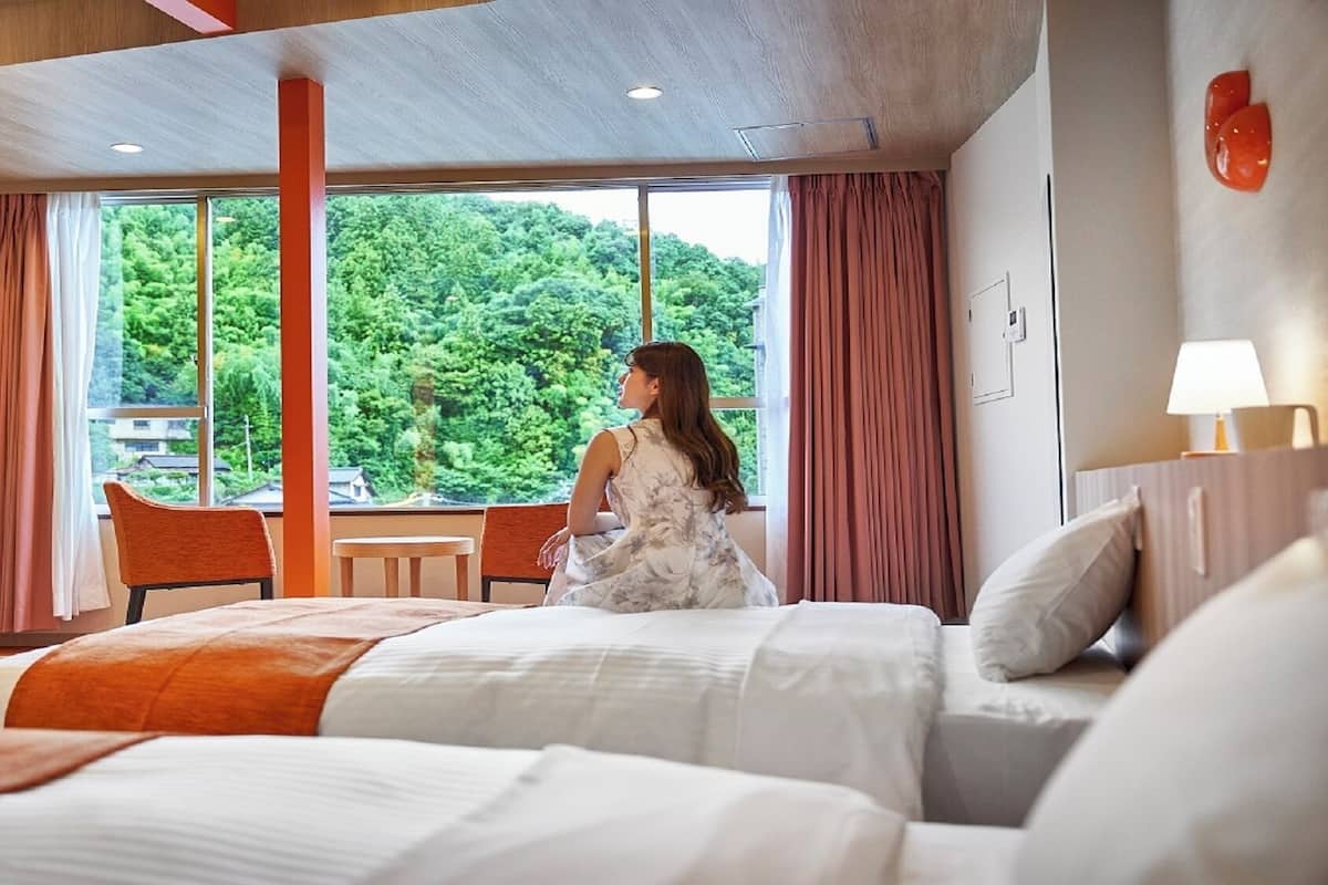 A hotel room with a bed, a chair, a table, and a large window with a view of greenery.