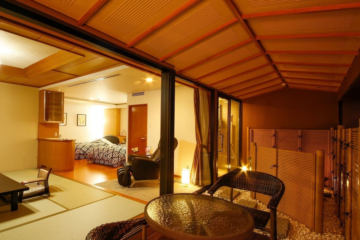 A traditional Japanese-style room with tatami flooring, a low table, a chair, and a sliding door leading to another room.