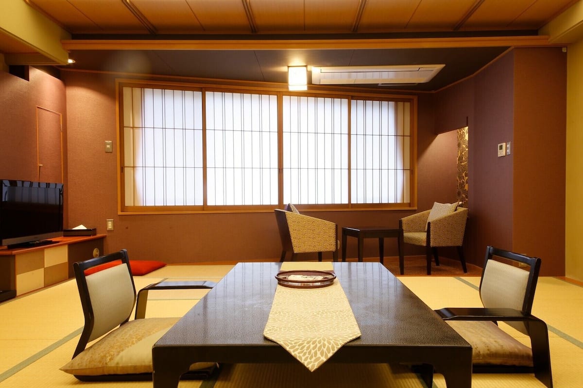 A traditional Japanese-style room with tatami flooring, a low table with a woven mat, and sliding shoji doors.