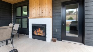 A modern outdoor seating area with a fireplace, wooden ceiling, and a door leading to a backyard. - Modern on Main-Walking Distance to Downtown Hill City and Mickelson Trail! (Hill City)