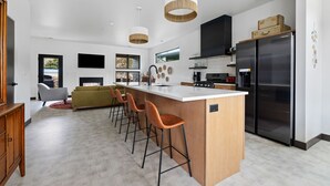 A modern kitchen with a central island, bar stools, a large refrigerator, and pendant lighting. - Modern on Main-Walking Distance to Downtown Hill City and Mickelson Trail! (Hill City)