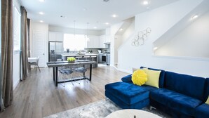 Ein modernes Wohnzimmer mit einem blauen Sofa, einem Essbereich mit Tisch und Stühlen sowie einer Küche im Hintergrund.
