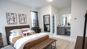 Ein modernes Schlafzimmer mit einem großen Bett, einer Bank und einem angrenzenden Badezimmer.